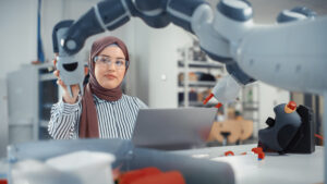 Modern Office: Portrait of Muslim Businesswoman Wearing Hijab and Working on Engineering Project, Coding on Laptop and Changing Robot Hand Position. Empowered Engineer With Startup Project.