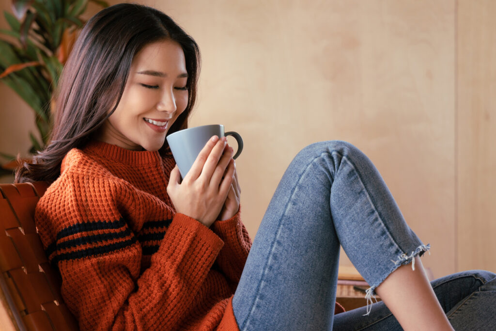 Portrait of a young Asian woman wearing a sweater. She inhaled the scent and drank the winter morning coffee. She smiles and enjoys being relaxed at home.