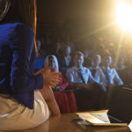 Rear view of beautiful businesswoman sitting with a laptop and discussing with the audience