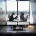 Young indian businessman ceo hr director having interview hiring for job with female African American attorney sitting in office at panoramic view window. Shot through jalousie glass.