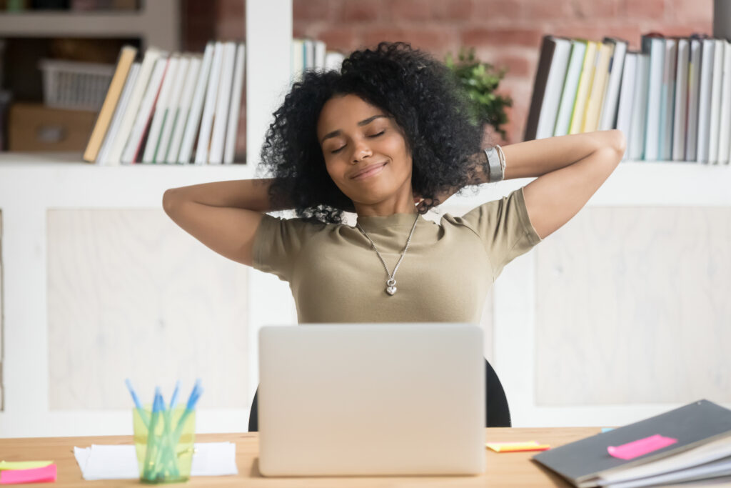 Calm African American businesswoman with hands behind head relaxing in comfortable office chair at workplace during break, satisfied female employee with closed eyes daydreaming about good future