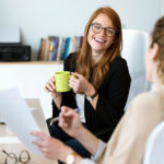 Shot of two pretty young business woman relaxing one moment while drinking coffee in the office.