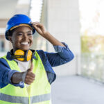 Cheerful young female engineer on a harbor showing thumb up. Cheerful female engineer smiling with giving thumbs up as sign of Success. Engineer woman holding thumbs up outdoor