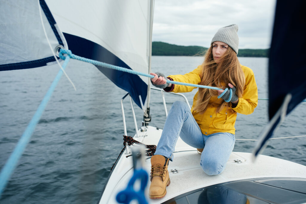 Young strong woman sailing the boat, pulling rigs and ropes on the bowspit