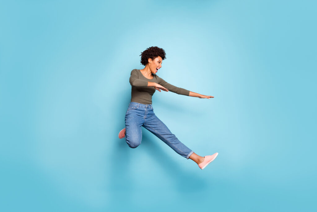 Full length photo of dark skin pretty wavy lady jumping high dancing, modern youngster moves wear casual outfit isolated pastel blue color background